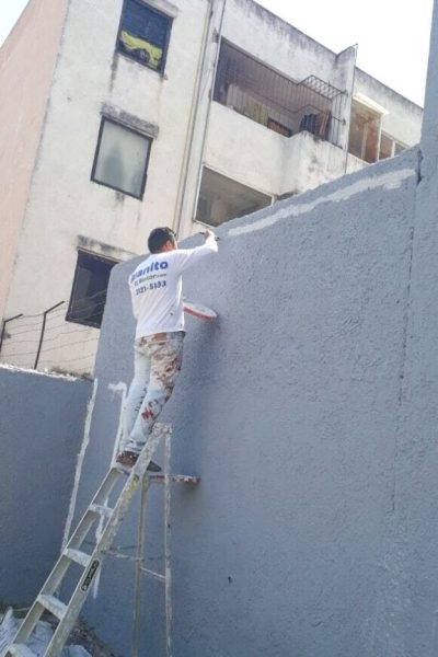 pintor de casas pintando la pared de un patio de color gris