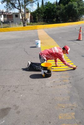pintor de casas pintando una zona de parada de autos de color amarillo con rallas sobre el asfalto