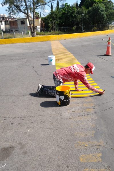 pintor de casas pintando una zona de parada de autos de color amarillo con rallas sobre el asfalto